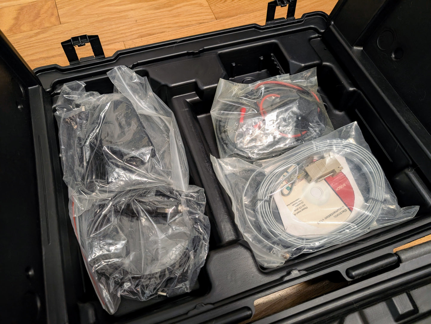A black hard case with assorted electronic cables, accessories, and a CD—organized in compartments—for the Vetronix TESTED Tech 2 Automotive Diagnostic Tool & Accessories for 1991-2013 GM vehicles.