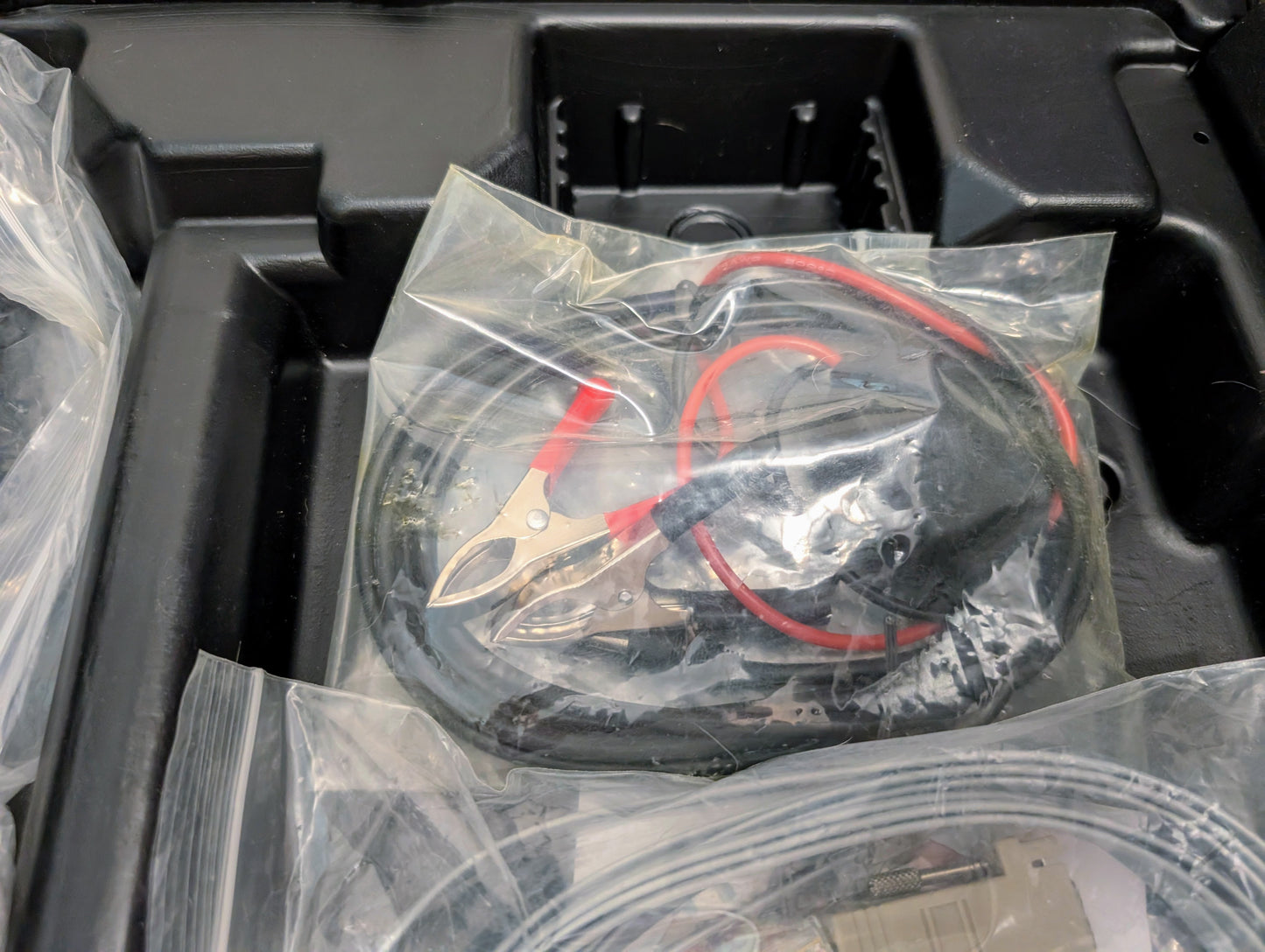 A coiled black cable with red and black alligator clips, sealed in clear plastic and packed in a molded compartment—ideal accessory for your Vetronix TESTED Tech 2 Automotive Diagnostic Tool & Accessories for 1991-2013 GM Vehicles.