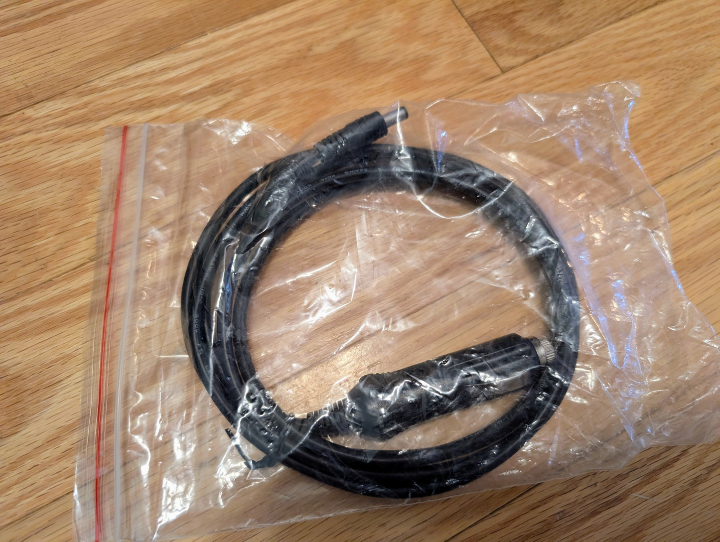 A black Vetronix audio cable with two connectors, compatible with the TESTED Tech 2 Automotive Diagnostic Tool & Accessories for 1991-2013 GM Vehicles, is coiled and sealed in a clear ziplock bag on a wooden surface.