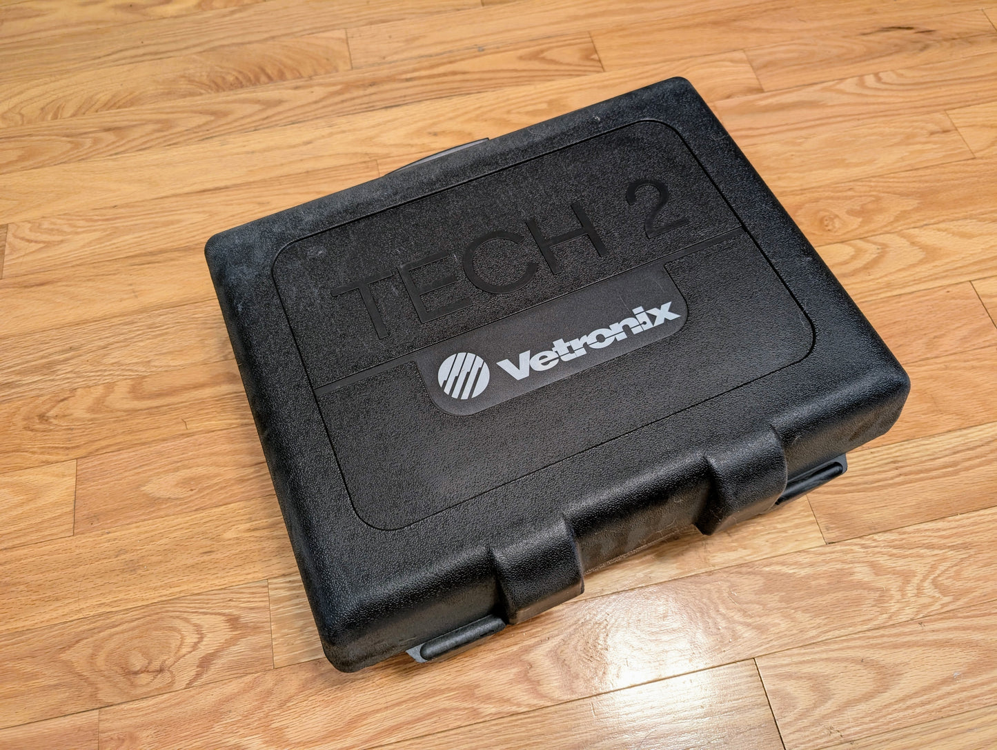 A black plastic carrying case labeled Vetronix holds the TESTED Tech 2 Automotive Diagnostic Tool & Accessories for 1991-2013 GM Vehicles, and sits closed on a wooden floor.