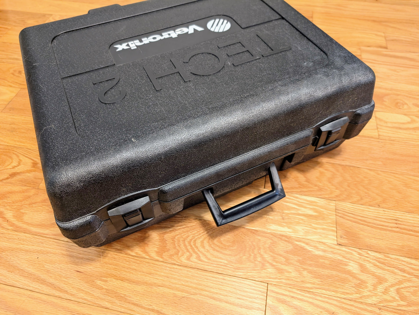 A black plastic Vetronix case with handle and secure latches sits on a wooden floor, labeled TECH 2—ideal for storing your TESTED Tech 2 Automotive Diagnostic Tool & Accessories for 1991-2013 GM Vehicles.
