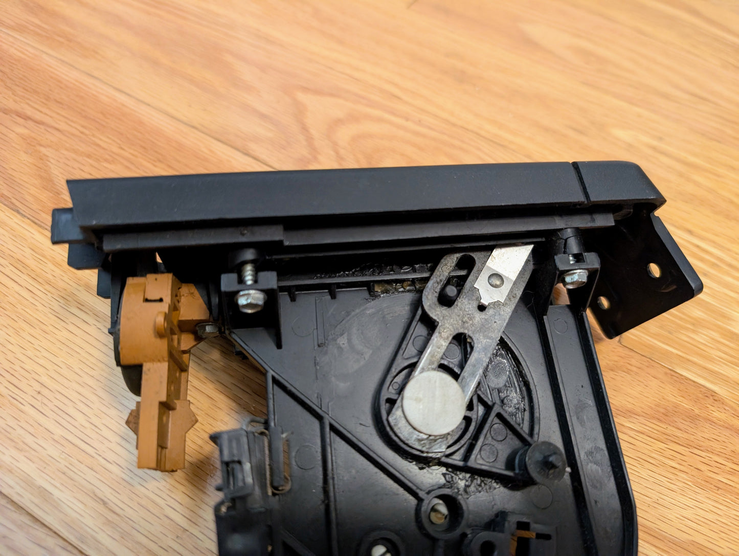 A close-up of a black plastic General Motors RARE HVAC Heater Control Panel OEM (no A/C, no vent) for 1986-1994 Chevrolet S10 and Blazer, with metal parts and screws, resting on a light wooden surface.