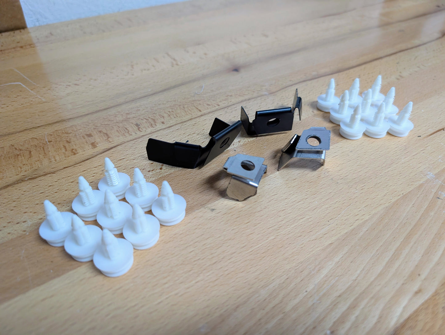Several white plastic fasteners and three metal clips from The Ugly Truckling KIT Door Panel Armrest Repair w/Clips for 1998-2005 Chevy S10, Blazer, GMC Sonoma, Jimmy are arranged on a light wooden surface, with the clips in the center.
