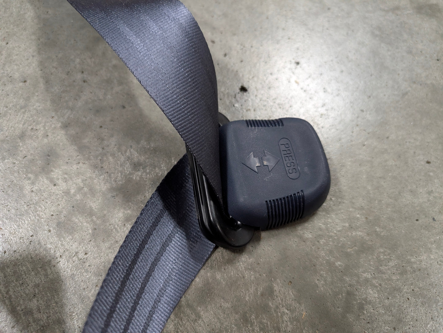 A close-up of a blue General Motors NOS passenger seat belt retractor & buckle for 1988-1994 Chevy/GMC C/K trucks, showing the "PRESS" label and arrow on the button.