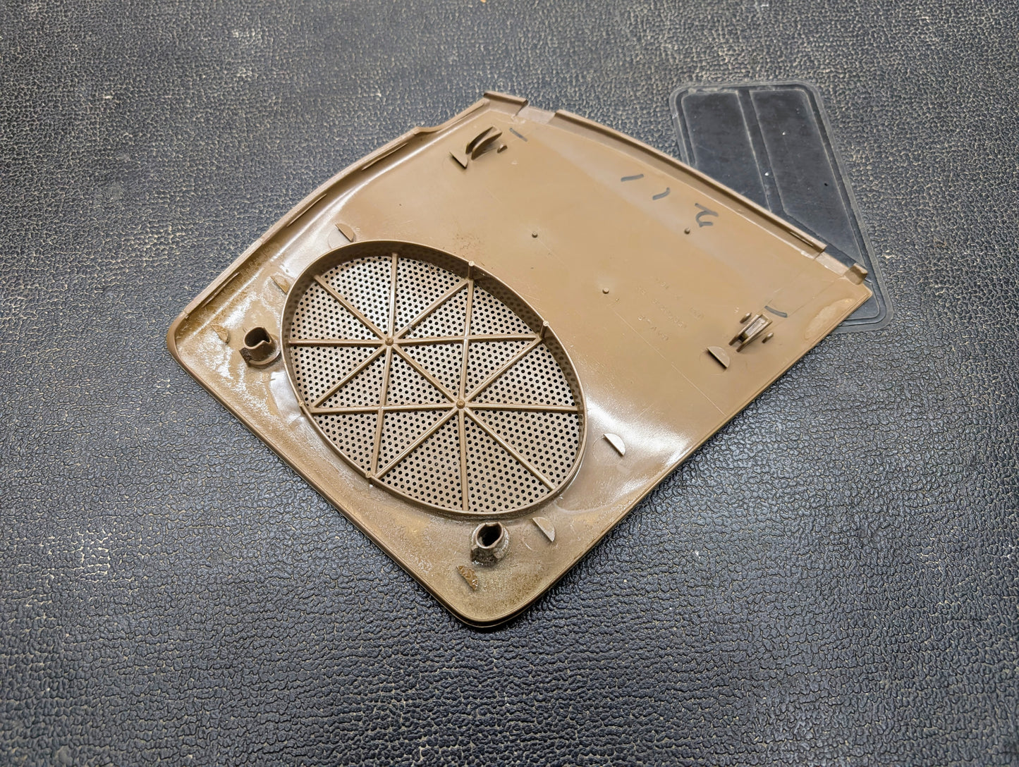 A beige OEM General Motors RH dash speaker grille cover for 1995-1997 Chevrolet S10, Blazer, and more features an oval perforated center, small clips, and raised edge patterns, shown on a textured black surface.