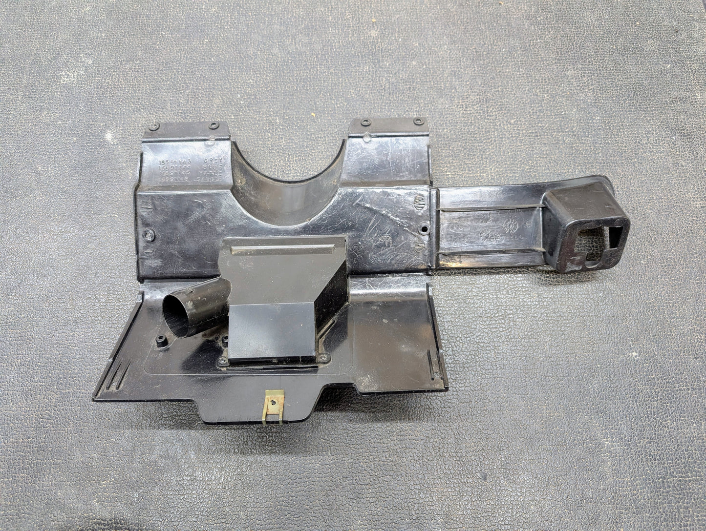 A General Motors OEM Lower Dash Trim Knee Bolster in dark gray for 1986-1993 Chevy S10, Blazer, GMC S15 and more, featuring multiple compartments and mounting points, is shown on a textured dark surface.