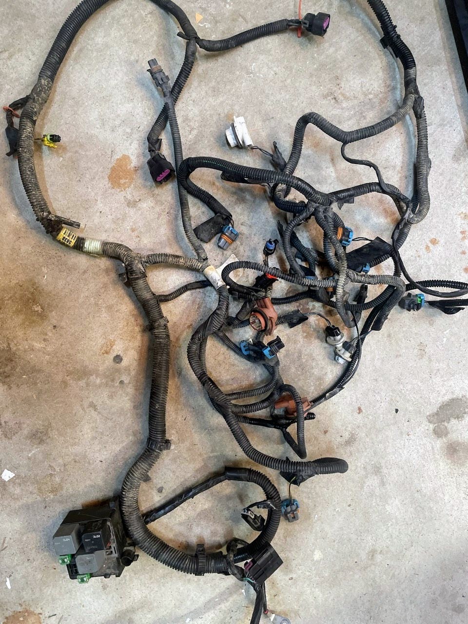 A used General Motors KIT Electric Fan Kit with Factory Harness for 1999-2006 GM Full Size Trucks, featuring bundled, black-tubed wires and connectors, is spread out on a concrete floor—ideal for your electric fan upgrade.