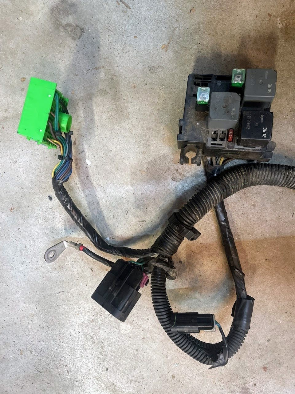 The General Motors KIT Electric Fan Kit with Factory Harness for 1999-2006 GM Full Size Trucks features multiple connectors like green and black plugs plus a fuse/relay box, shown here on a concrete surface—ideal for an electric fan upgrade.