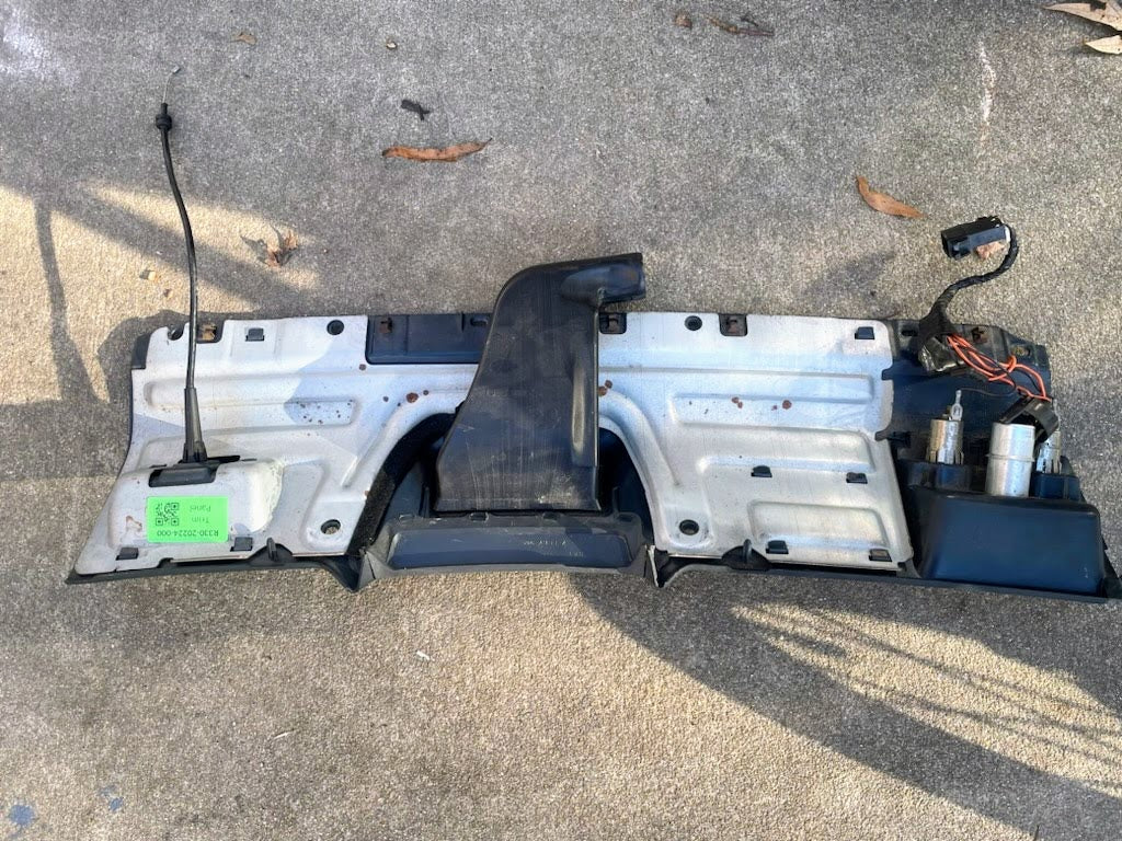 A blue General Motors Lower Dash Trim Knee Bolster for 1995–1997 Chevy S10 Blazer and more, with wires, connectors, and a black air duct, lies on concrete among dry leaves.