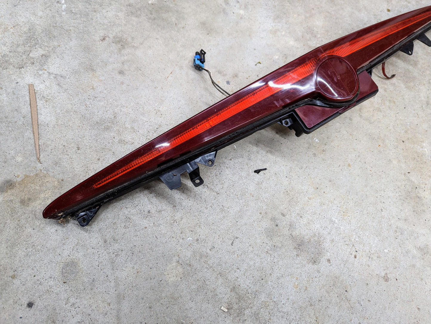 A General Motors OEM Center High Mount Third Brake Lamp (CHMSL) for 2003-2007 Cadillac CTS, complete with wiring and connectors, rests on a concrete floor.