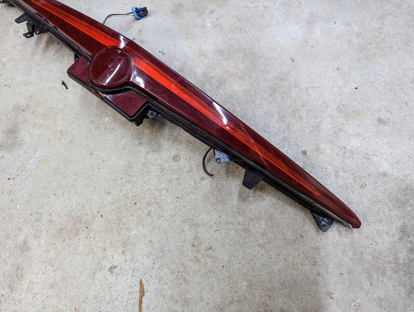 A General Motors OEM Center High Mount Third Brake Lamp (CHMSL) for 2003-2007 Cadillac CTS is lying on a concrete floor.