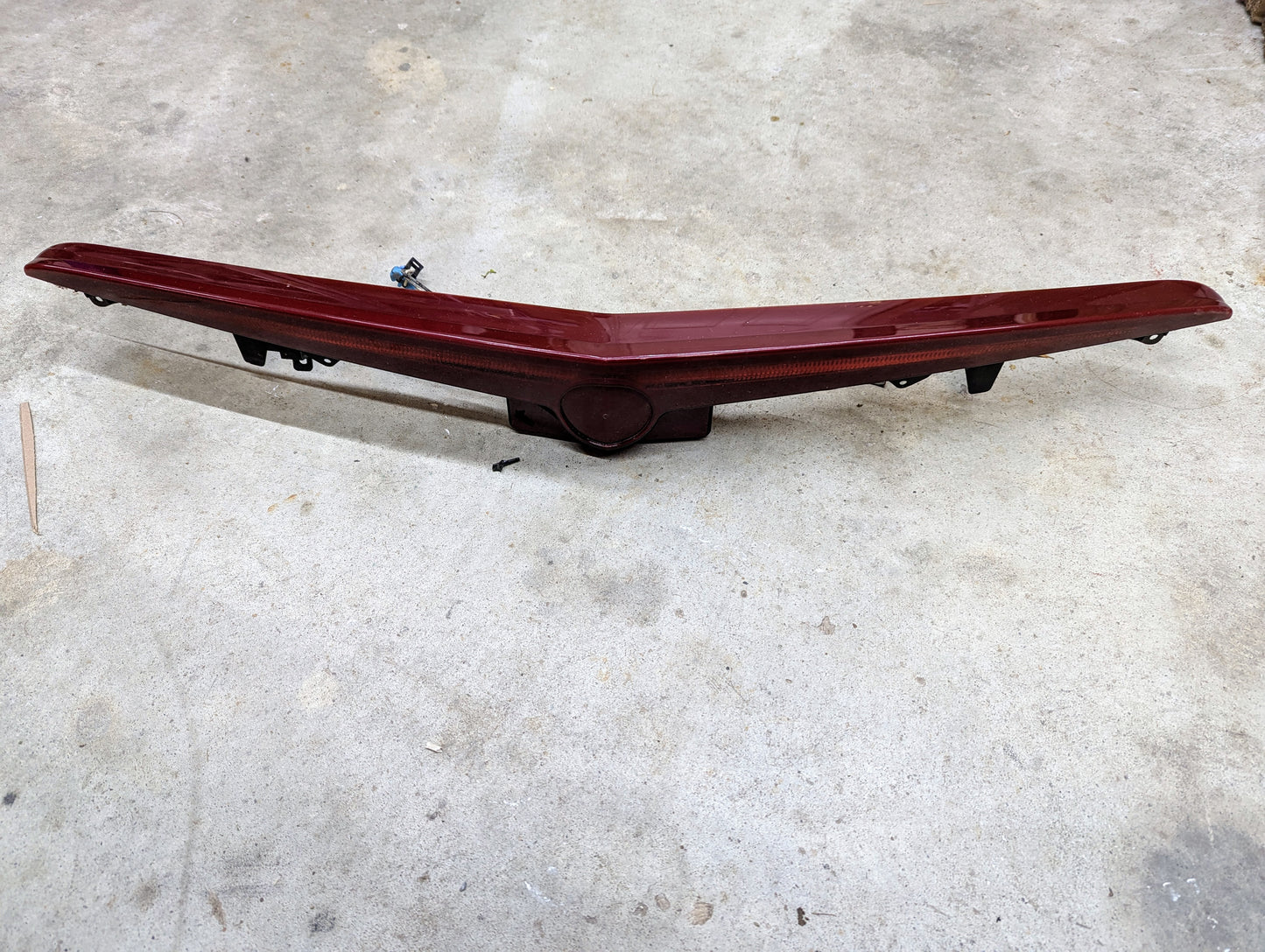 A clean, undamaged General Motors OEM Center High Mount Third Brake Lamp (CHMSL) for 2003-2007 Cadillac CTS with a slight V shape and a small top-center mounting bracket is placed on a concrete floor.