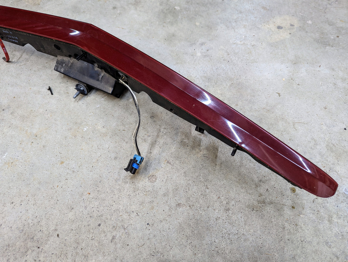 A General Motors OEM Center High Mount Third Brake Lamp (CHMSL) for 2003-2007 Cadillac CTS, with wiring connector and exposed mounting brackets, is shown detached on a concrete floor.