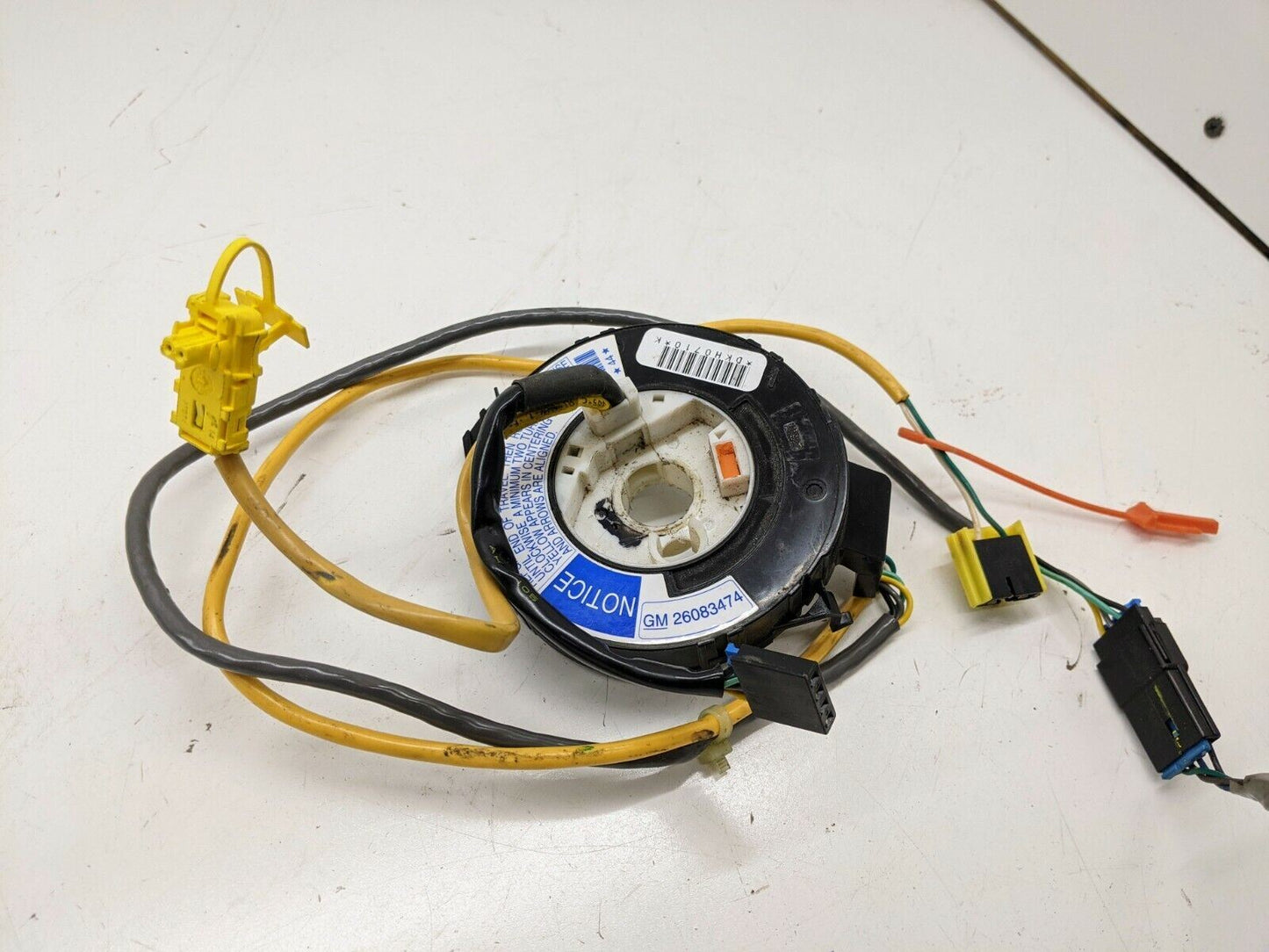 A General Motors OEM Steering Wheel SRS Air Bag Clock Spring, tested with radio controls for 2000-2003 Chevy S10 Blazer, features yellow, black, and orange wires plus multiple connectors. A blue label and barcode appear on the black component.