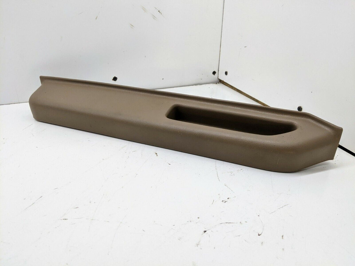 A beige plastic General Motors OEM door panel armrest handle for 1986-93 Chevy S10 Blazer or GMC Jimmy, shown on a white surface with scuff marks; fits driver side as a replacement NOS part.