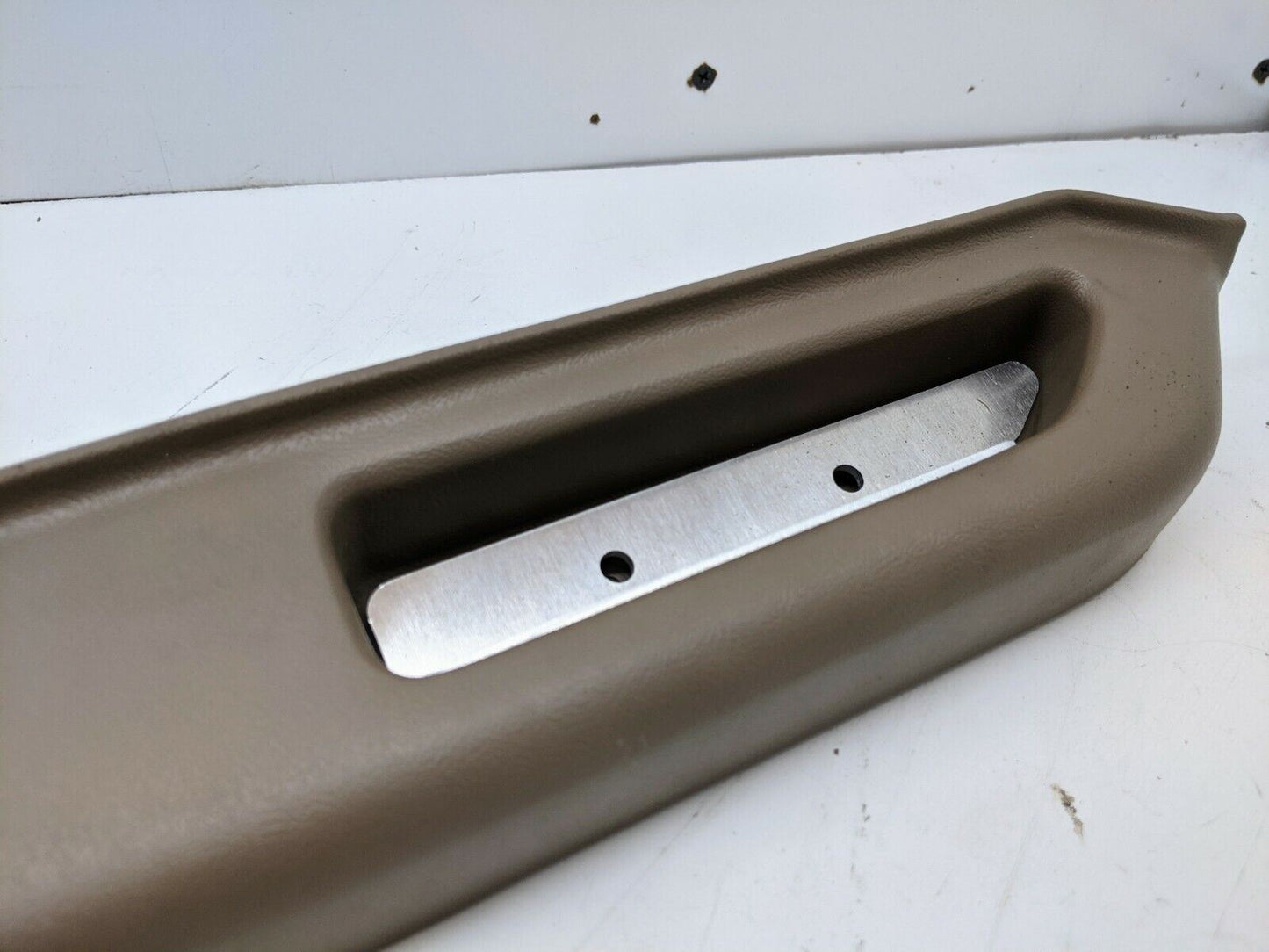A close-up of the KIT Door Panel Armrest Repair w/Hardware by The Ugly Truckling for 1986-1993 Chevy S10, Blazer, GMC S15, and Jimmy shows a brown rectangular part with a recessed handle and metal plate against a white background.