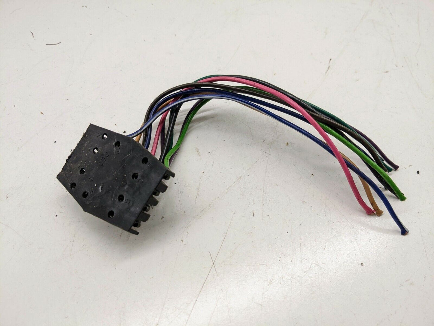 A black rectangular 10 Pin Power Window Switch Wiring Harness Connector Plug by General Motors has blue, green, purple, red, and black wires and is compatible with GM S10 4 Button Master Switches. It is shown on a white surface.