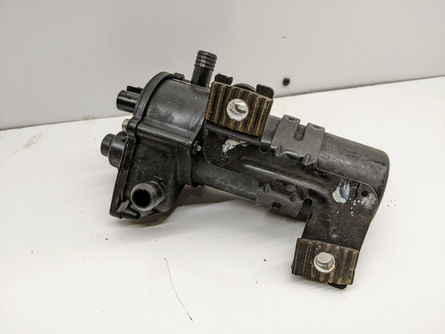 The OEM Brake Vacuum Booster Supplemental Assist Pump by General Motors is a black metal automotive part with connectors and mounting brackets, designed for 2003-2006 Chevy Silverado, Tahoe, GMC Sierra, Yukon and more. Shown on a plain white background.