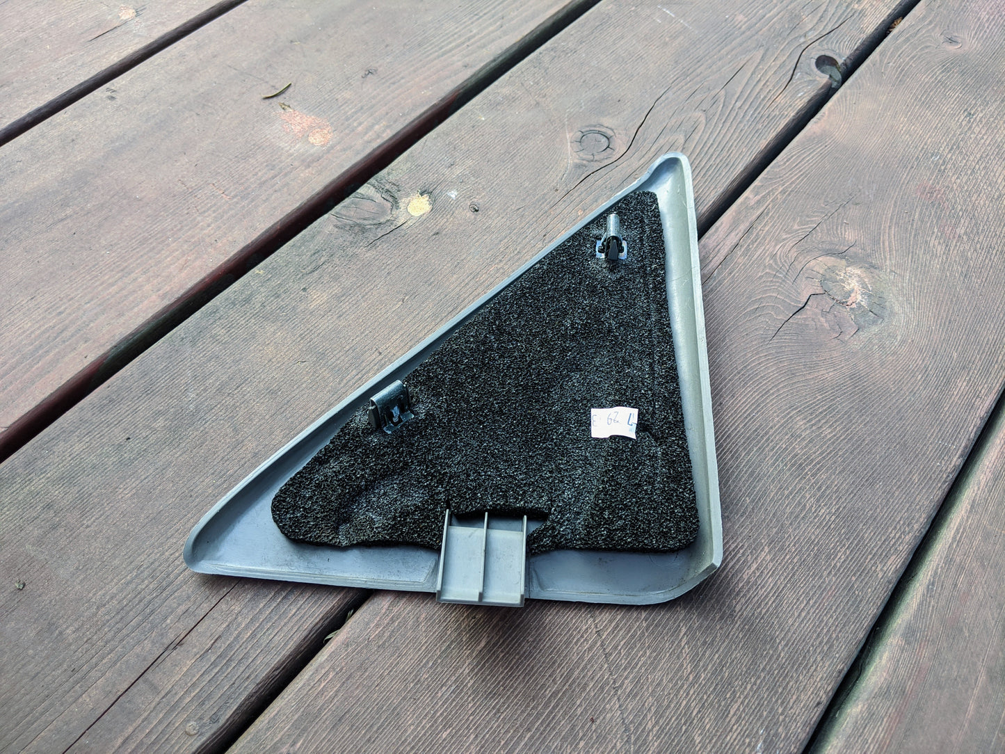 A General Motors Left Driver Sail Panel LH Mirror Trim Cover in Light Gray for 1999–2006 Silverado, Tahoe, Yukon, and more with clips and black felt backing sits on a wooden deck. A label marked 5.0 is attached to the felt surface.