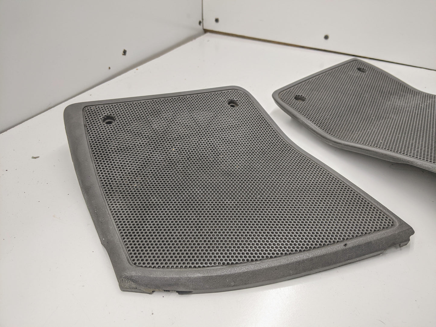 A pair of General Motors OEM LH RH dash speaker grille covers in light gray, designed for 1995–1997 Chevrolet S10, Blazer, and more, are displayed on a white surface against a white wall. One cover is fully visible while the other is partially shown.