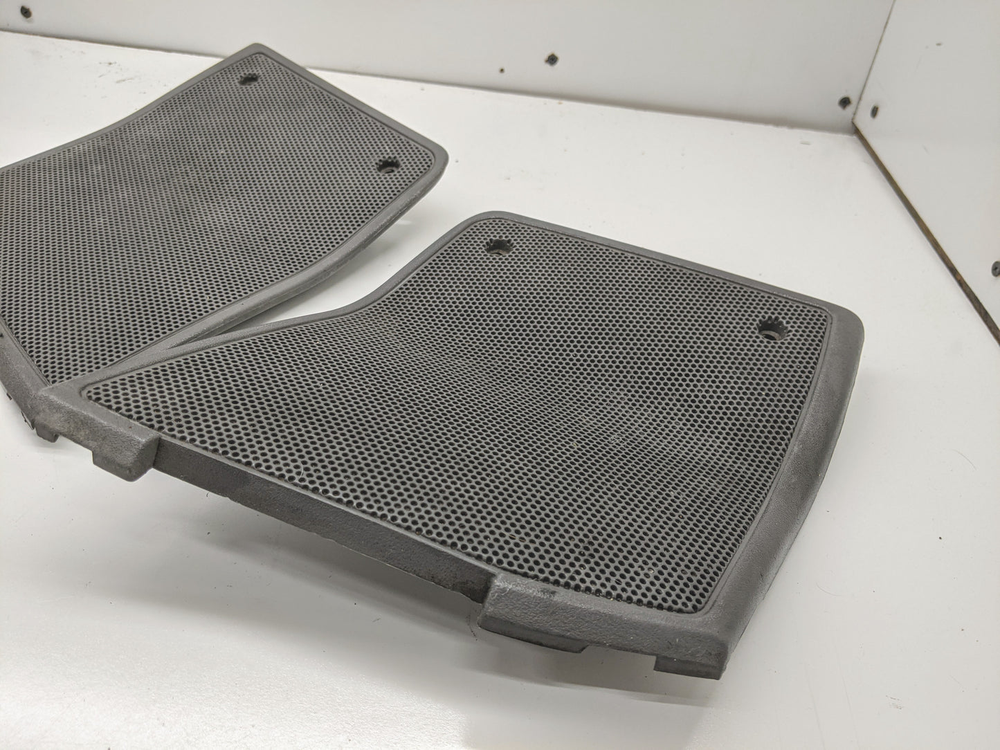 A pair of light gray OEM General Motors dash speaker grille covers for 1995-1997 Chevrolet S10, Blazer, and more, shown on a white surface leaning against a white wall.