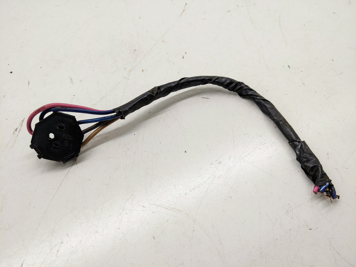 The General Motors OEM Power Window Switch Wire Connector Pigtail features four colored wires and a black circular connector, with exposed wire tips and black tape—perfect for 80s/90s GM models including S10, Camaro, Buick, Cadillac, and more.