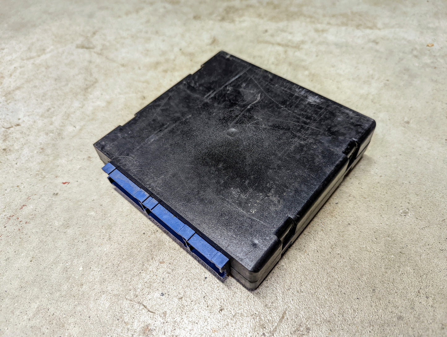 A black plastic General Motors BCM Body Control Module 09372445 with blue connectors, suitable for 1998-2000 Chevy S10, Blazer, GMC Sonoma, Jimmy, and Bravada, shown on a light-colored concrete surface.