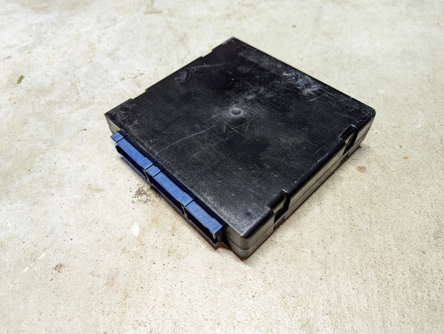 A black, rectangular plastic General Motors BCM Body Control Module 09371990 with blue latches sits on rough, light-colored concrete; it looks slightly worn and fits 2000-2001 Chevy S10, Blazer, Astro, GMC Yukon, Jimmy, and more.
