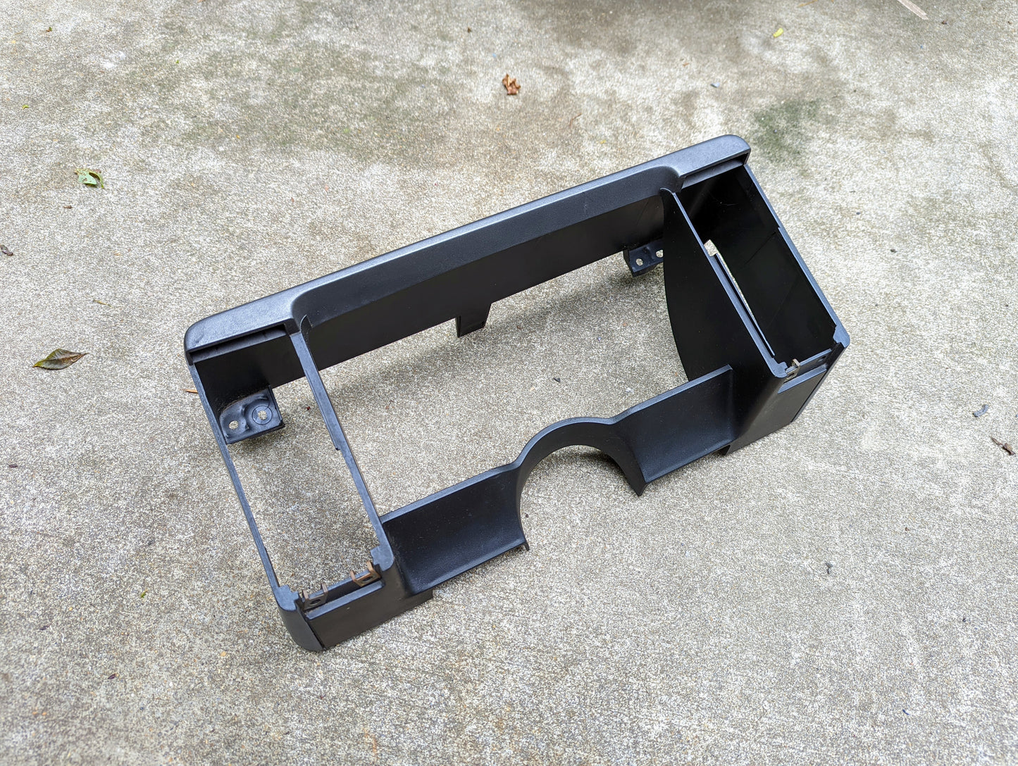 A General Motors OEM Gray Instrument Cluster Dash Bezel for 1986-1993 Chevy S10, Blazer, GMC S15 and more is shown on rough concrete. Rectangular with cutouts and side brackets, it’s the perfect factory-fit interior bezel for your vehicle.