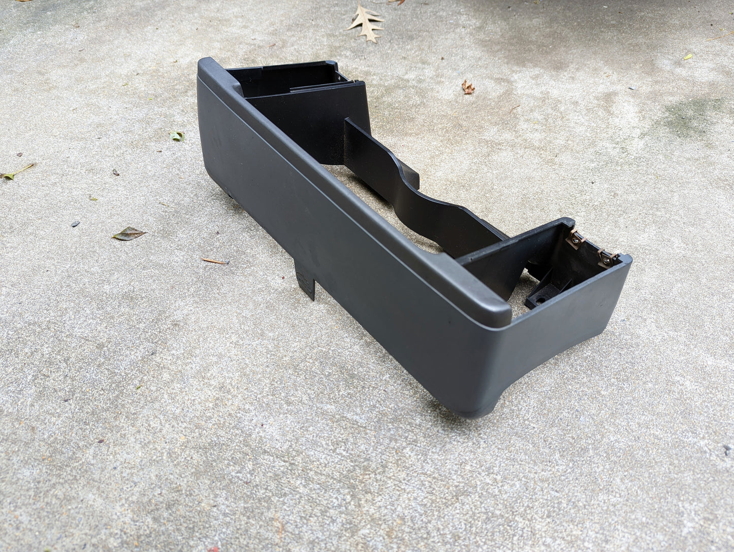 A gray OEM Instrument Cluster Dash Bezel by General Motors for 1986–1993 Chevy S10, Blazer, GMC S15, and more rests on a concrete surface outdoors with a few small leaves scattered nearby.