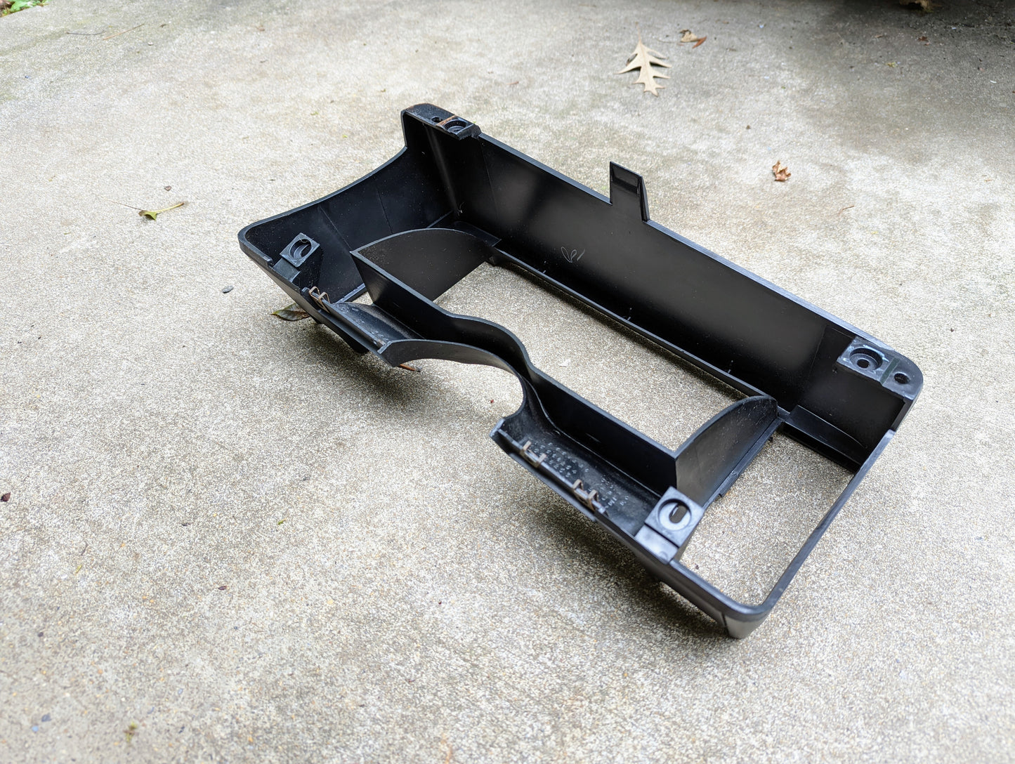A General Motors OEM gray instrument cluster dash bezel for 1986-1993 Chevy S10, Blazer, and GMC S15 rests on light concrete, with small leaves nearby.