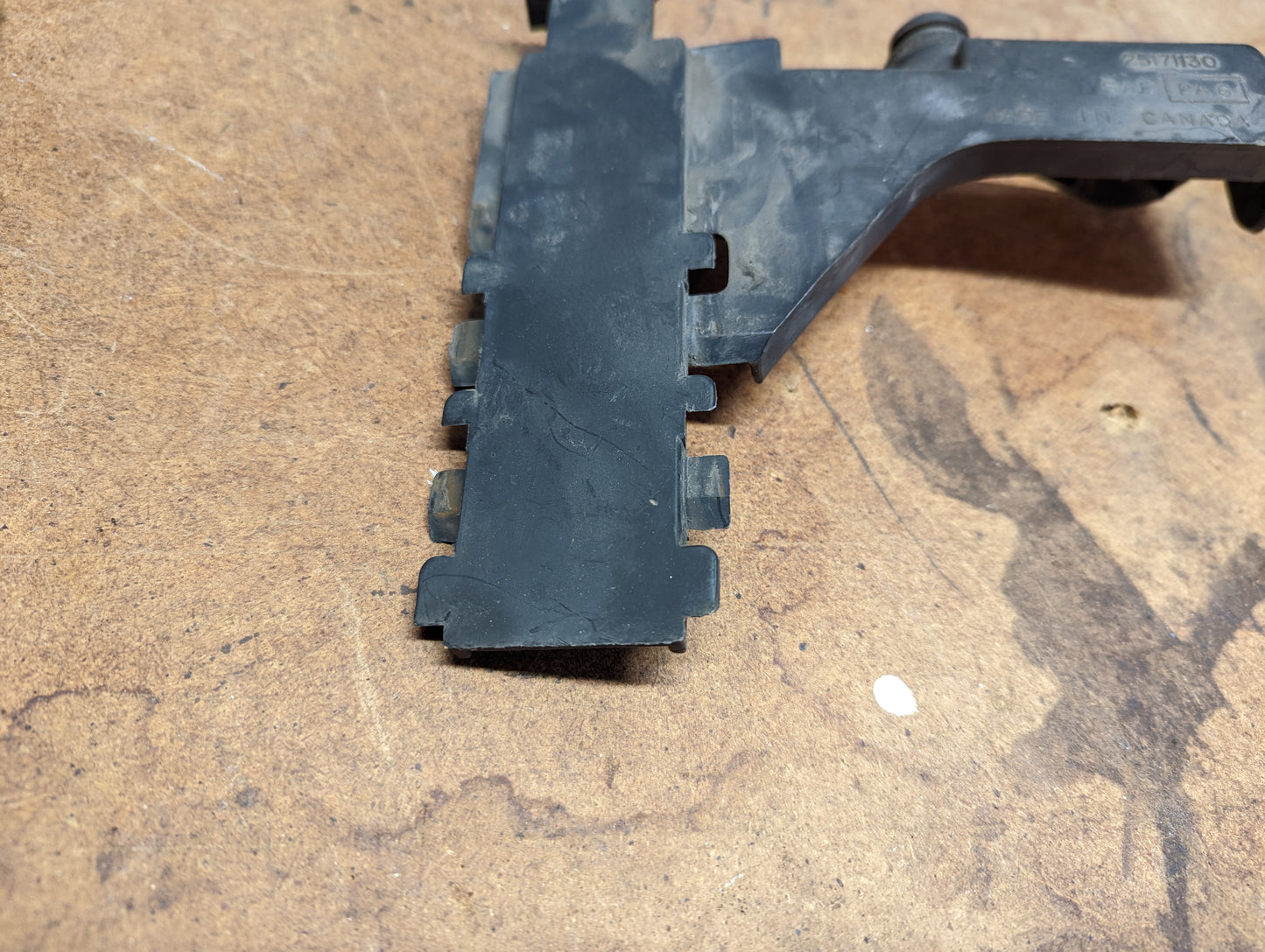 A close-up of a General Motors OEM Cold Air Intake Filter Box to Core Support Bracket for 1996-2005 Chevrolet S10, Blazer, and more, shown on a brown stained wooden surface.