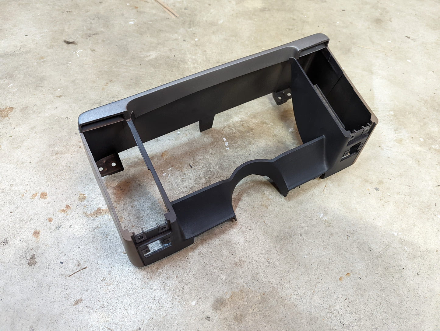 A General Motors OEM Instrument Cluster Dash Bezel in tan for 1986-1993 Chevy S10, Blazer, and GMC S15, with various rectangular cutouts, is displayed on a textured concrete floor.