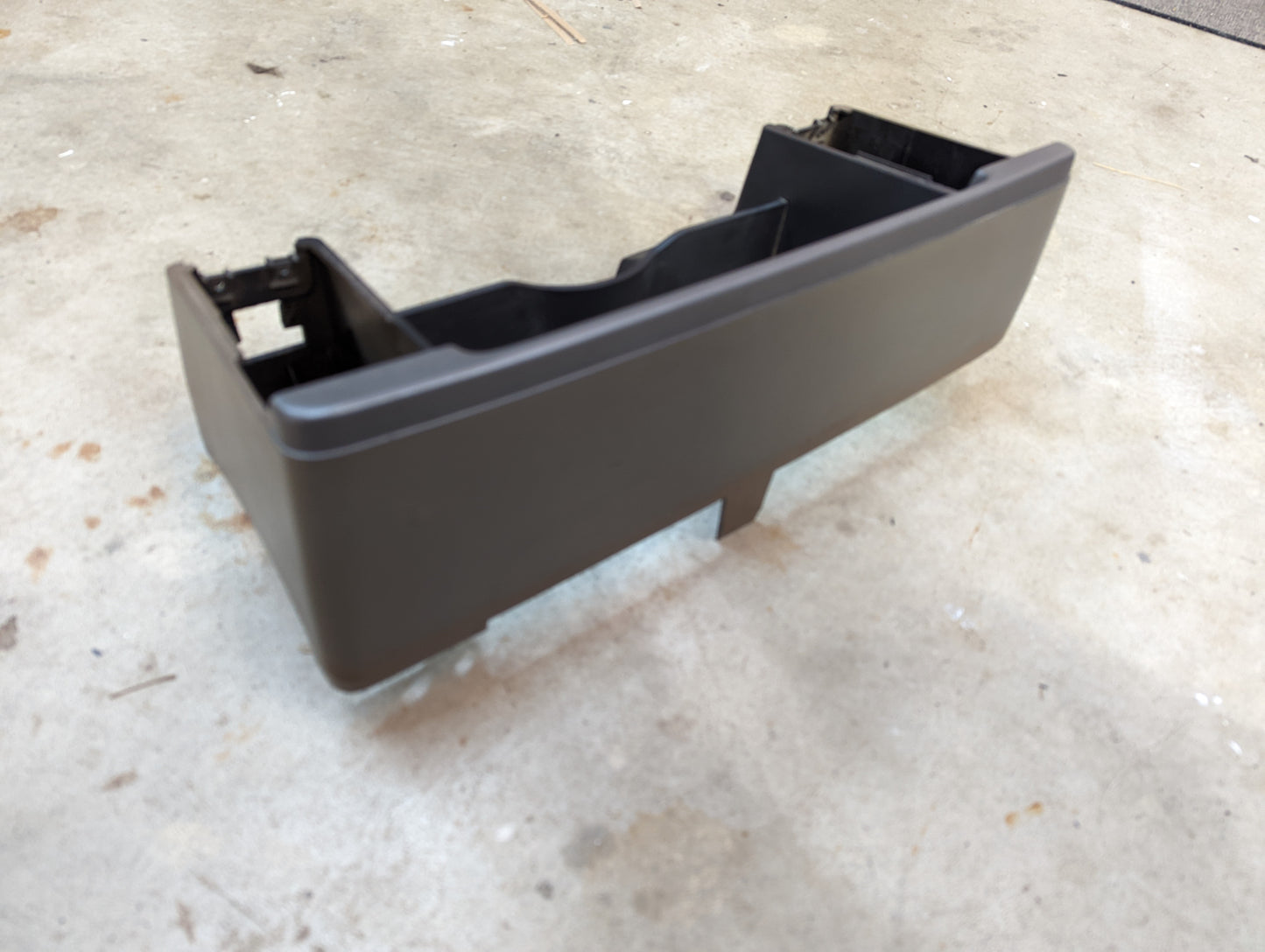 A General Motors OEM tan instrument cluster dash bezel for 1986-1993 Chevy S10, Blazer, GMC S15, and more sits on a speckled concrete floor. Molded edges and compartments suggest its meant for dashboard or console use.