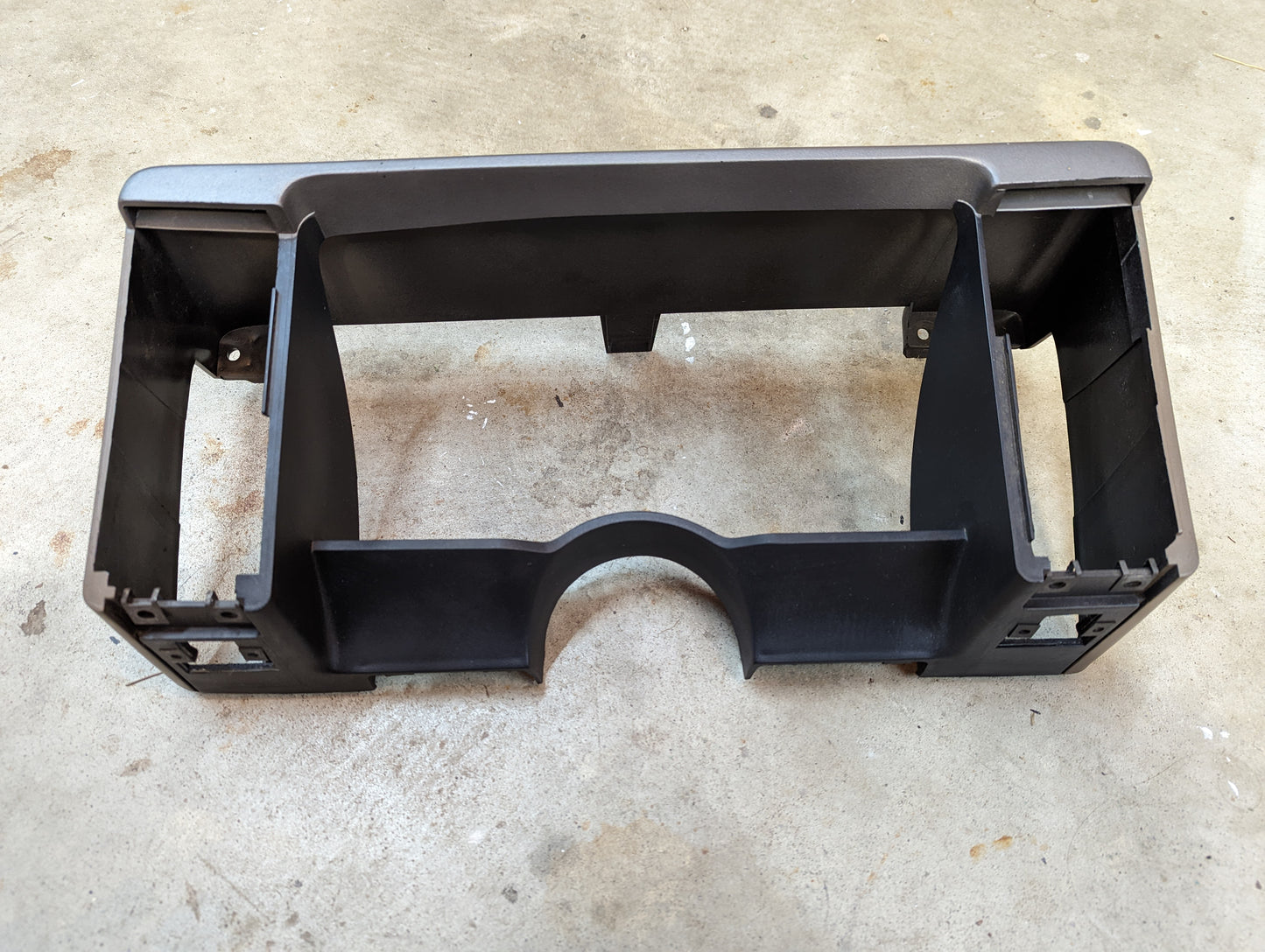 A tan OEM instrument cluster dash bezel by General Motors for 1986-1993 Chevy S10, Blazer, GMC S15 and more, featuring rectangular openings, mounting tabs, a curved bottom center; shown on concrete; fits beige interiors.