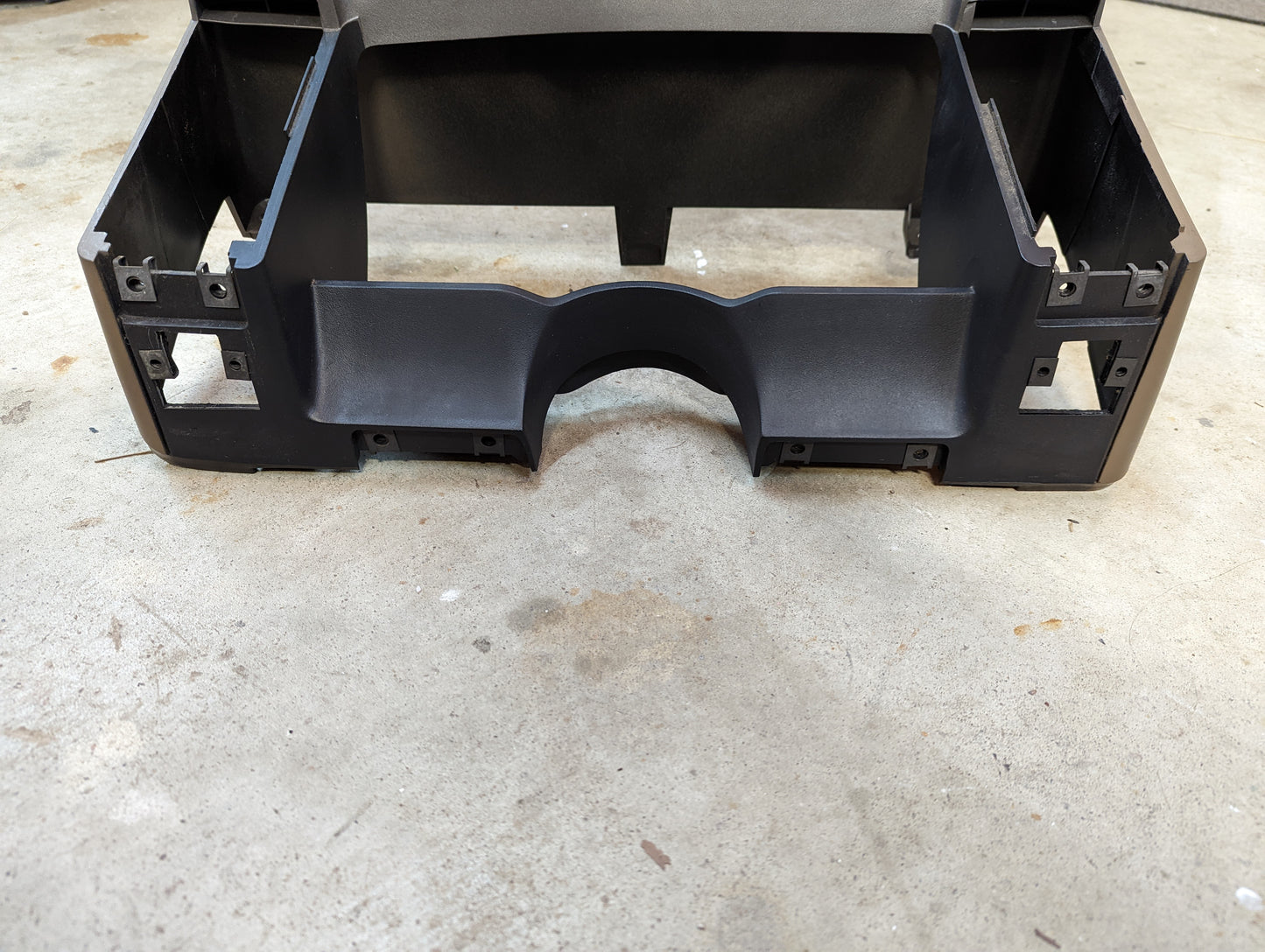 A tan plastic OEM instrument cluster dash bezel by General Motors for 1986-1993 Chevy S10, Blazer, GMC S15, and more sits on concrete, displaying the rear with multiple rectangular cutouts and mounting points.