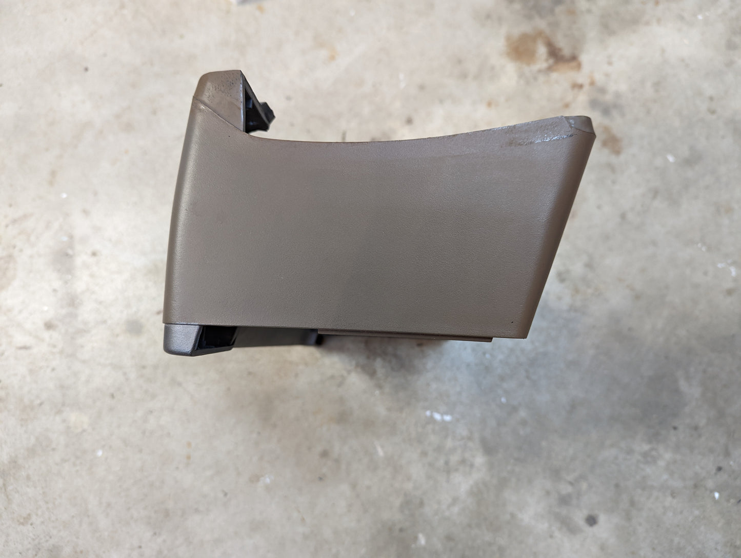 A General Motors OEM Instrument Cluster Dash Bezel in tan for 1986-1993 Chevy S10, Blazer, GMC S15, and more is shown on a concrete floor, viewed from above. The curved plastic trim piece fits beige interiors.