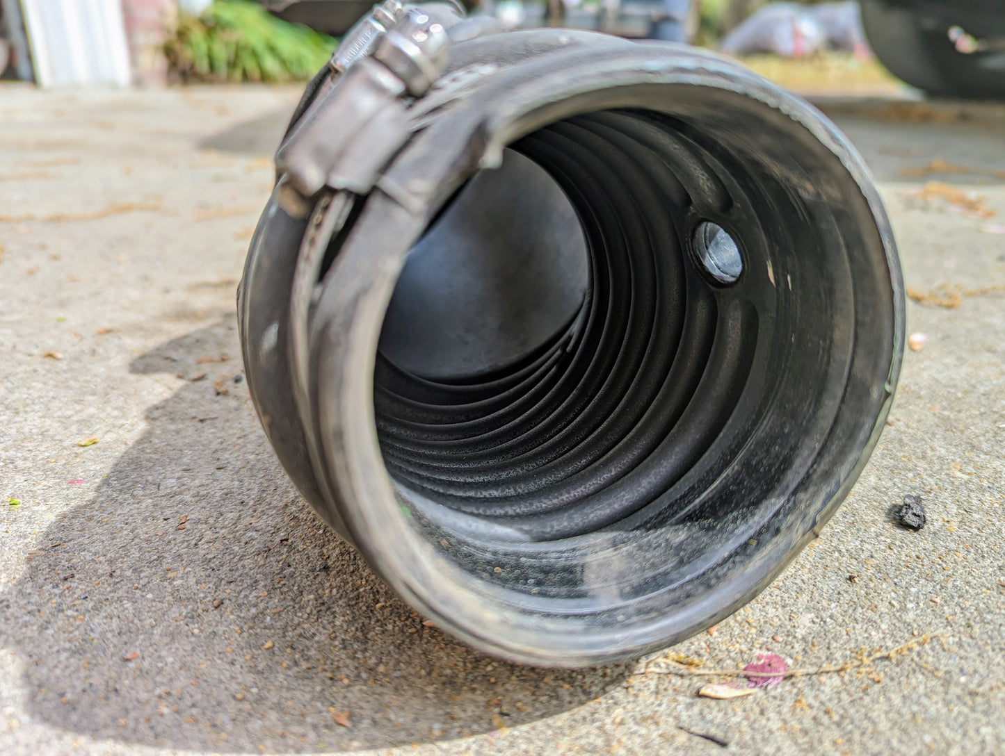 A close-up of a black, ribbed OEM Cold Air Intake Duct 25099892 by General Motors, with metal clamps, designed for 4.3L 1996–2005 Chevrolet S10, Blazer, and more—showing its hollow interior on a concrete surface.