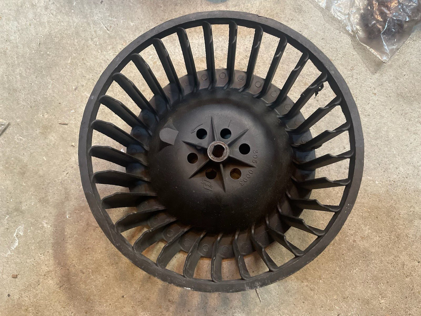 A black plastic or rubber airless tire with open sidewalls and a central hub sits on a concrete floor, resembling the durable components in General Motors OEM A/C Delete Heater Box & Control Panel Swap Parts for 1986-1994 S10, Blazer, and more.