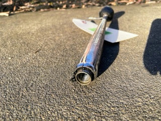 A close-up of a General Motors OEM 5 Speed Manual Transmission Shifter Handle for 1982-1993 Chevy S10 and Blazer, lying on concrete with the open end facing the camera and a product tag partially visible in the background.
