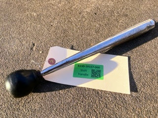 A General Motors OEM 5 Speed Manual Transmission Shifter Handle for 1982–1993 Chevy S10, Blazer, and more rests on a textured surface, partially covering a cream label with a green Safe Handle sticker and QR code.