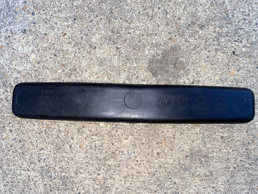 A black General Motors OEM Center Console Cup Holder Storage Bin Rubber Mat Liner for 2003-2006 Chevy Silverado/GMC Sierra features embossed text, including MADE IN CANADA and symbols, resting on rough light gray concrete.