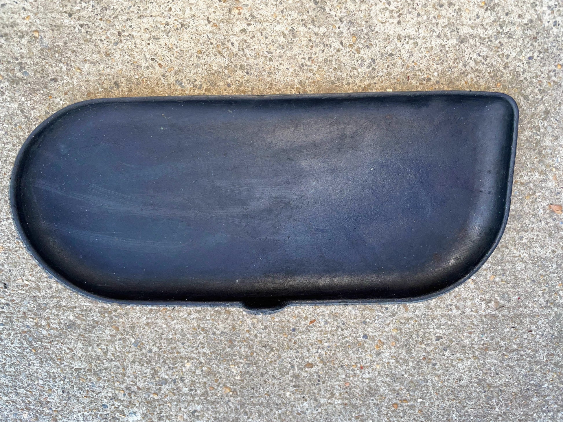 A black, rounded OEM Center Console Cup Holder Accessory Bin Driver Side Rubber Mat Liner by General Motors rests on gray concrete—solid and smooth, made for 2003-2006 Chevy Silverado, GMC Sierra, and more full size trucks.