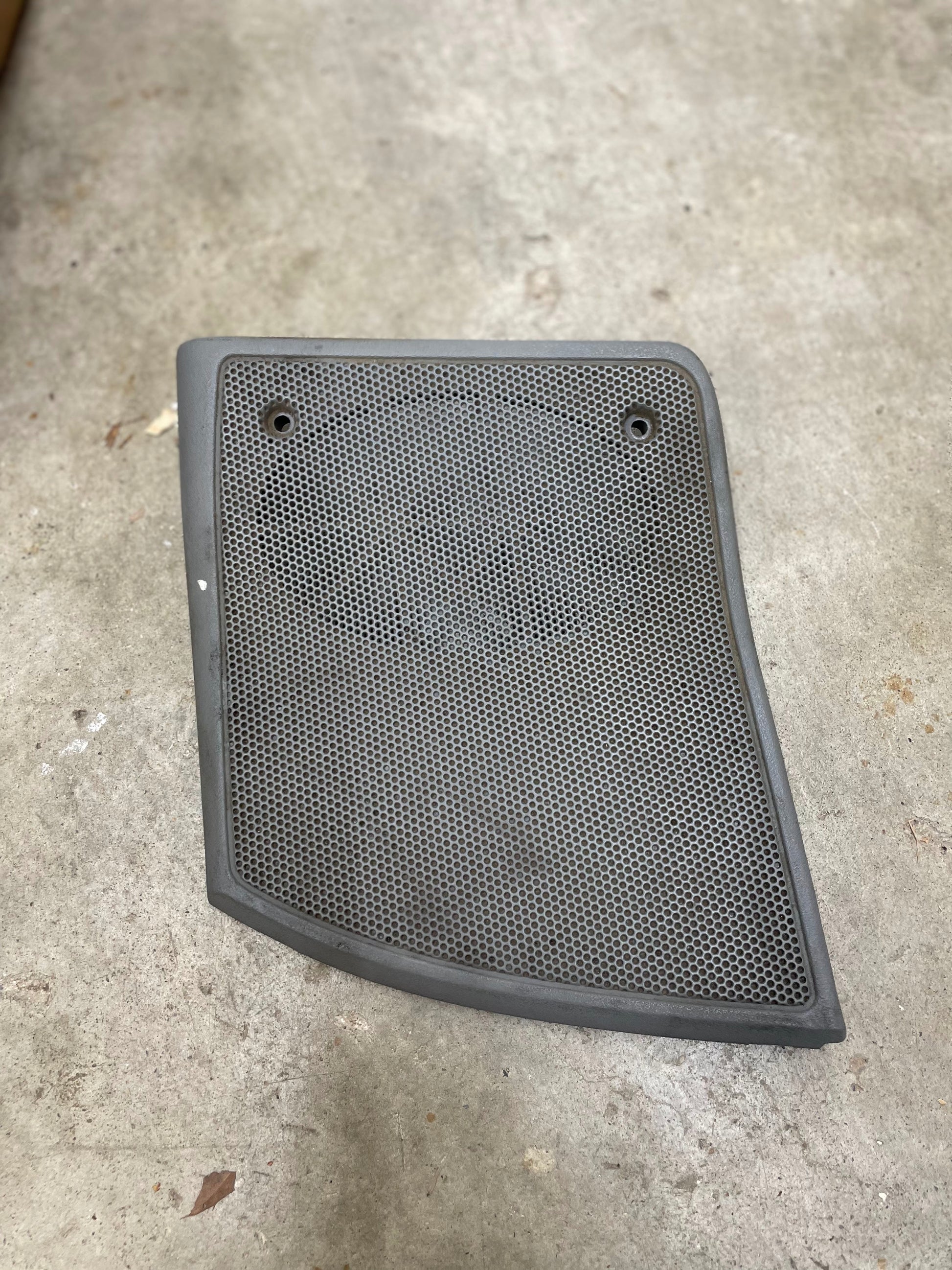 A light gray OEM Passenger RH dash speaker grille cover by General Motors with a broken tab, designed for 1995-1997 Chevrolet S10, Blazer, and more models, ideal for speaker maintenance.