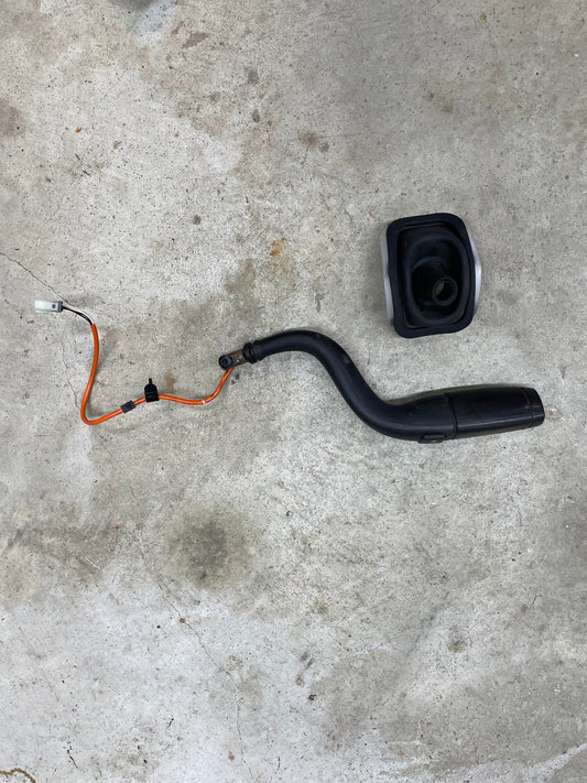 A General Motors OEM Column Shift Lever with Tow/Haul & Tapshift for 2006-2007 GM Duramax LBZ lies on a gray concrete floor next to its detached black plastic cover.