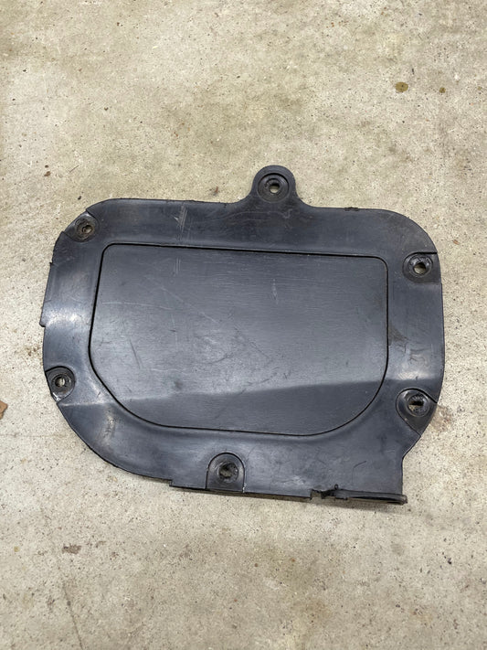 A black, irregularly shaped plastic OEM Fresh Air Block-Off Panel by General Motors for 1982–1993 Chevrolet S10, Blazer, and more with four screw holes and a flat rectangular center rests on a light-colored concrete surface.