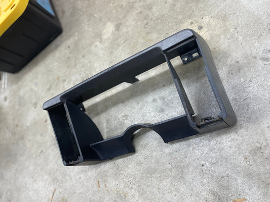 A gray General Motors OEM instrument cluster dash bezel for 1986–1993 Chevy S10 Blazer, GMC S15, and more sits on a concrete garage floor, featuring cutouts for gauges, vents, or controls.