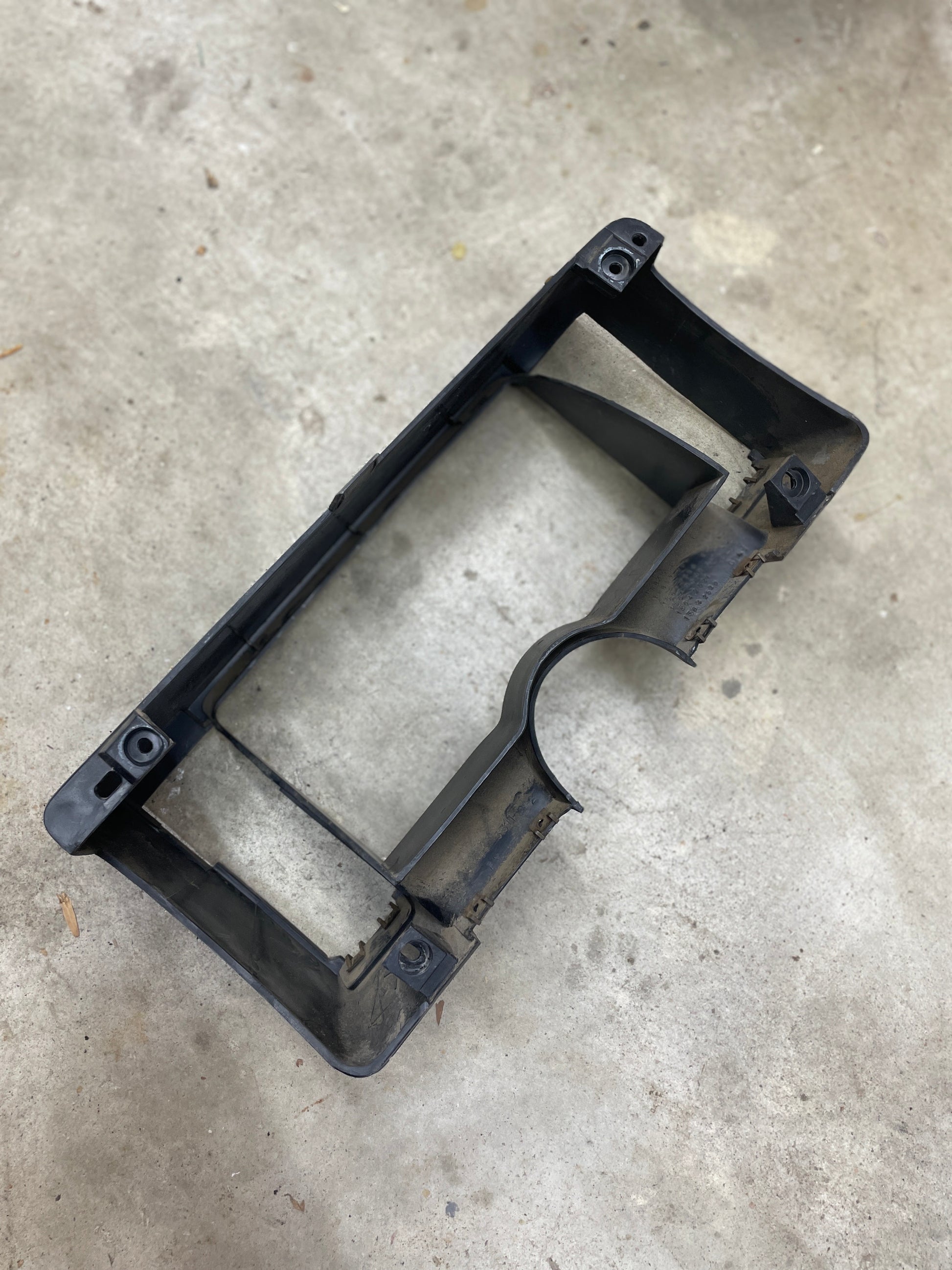 A used gray OEM Instrument Cluster Dash Bezel by General Motors for 1986-1993 Chevy S10 Blazer, GMC S15, and more is shown on a gray concrete floor with some dust and rust visible around the edges.