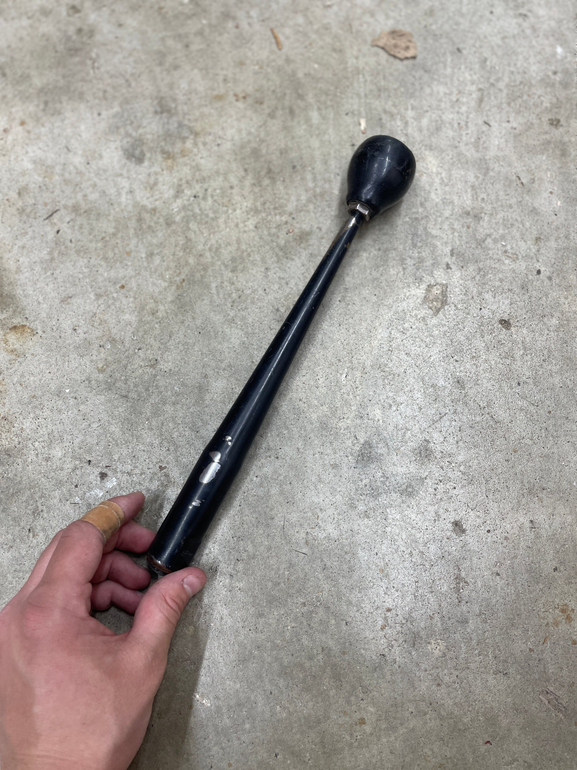 A hand holds a General Motors OEM 5 Speed Manual Transmission Shifter Handle for 1982-1993 Chevy S10, Blazer, and more, resting on a concrete floor.