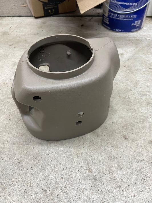 A General Motors SET Steering Column Shift Cover w/Automatic Transmission in Beige for 2001-2002 GMC Denali, Cadillac Escalade, and more rests on a concrete floor with paint cans and cardboard boxes in the background.